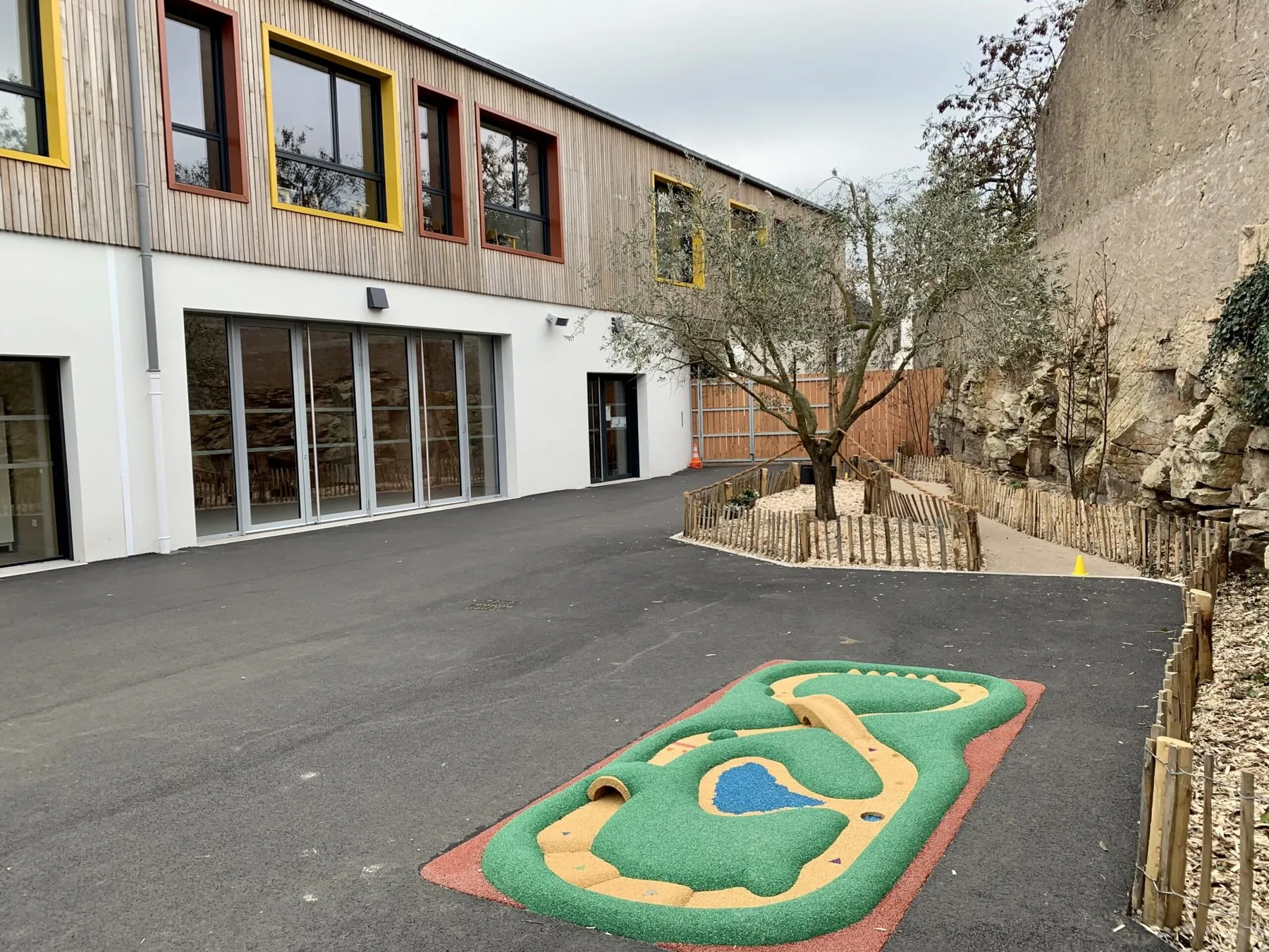 La cour de l'école neuve, son olivier et sa façade en bois.