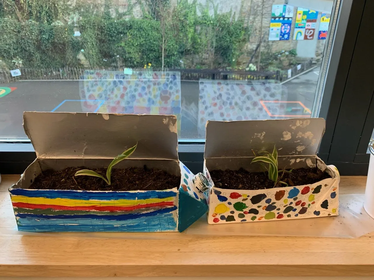 Des jardinières peintes par les élèves de CM, devant une baie vitrée.