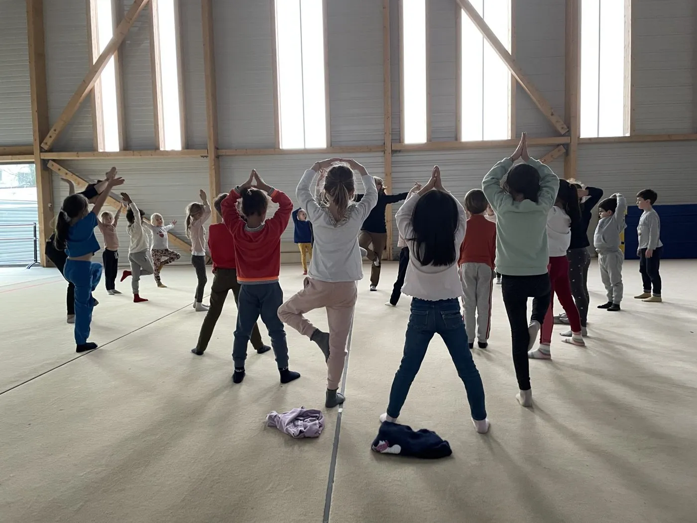 Des élèves de dos, bras levés, pendant l'échauffement dans la grande salle de gymnastique.