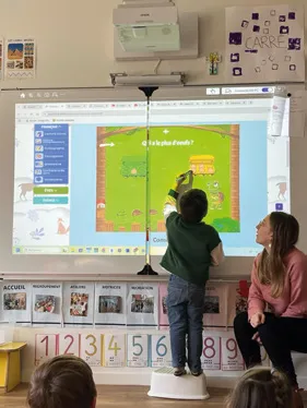 Un élève, de dos, montre une réponse au tableau numérique de sa classe.